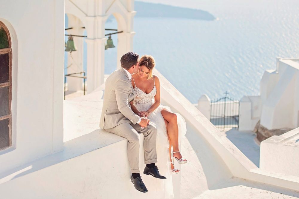 Couple sits on white-washed steps overlooking the Mediterranean Sea and iconic Santorini architecture.