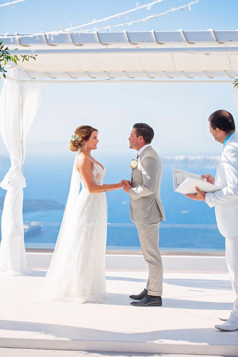 A bride and groom share their first dance together on a white terrace overlooking a serene ocean view.