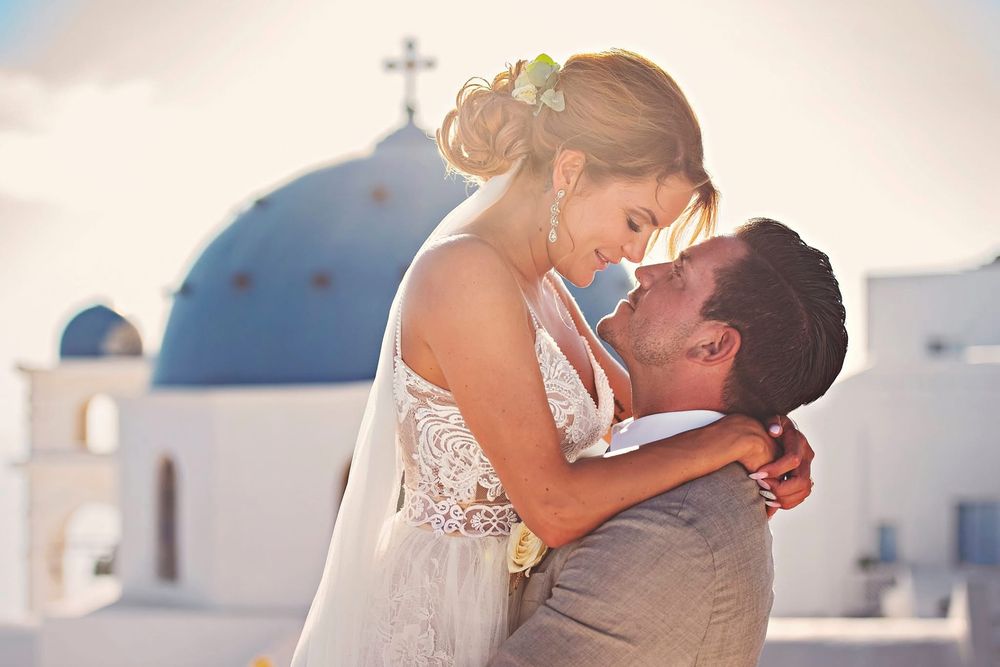Romantic couple embrace during their destination wedding in Santorini with white church domes in the background.