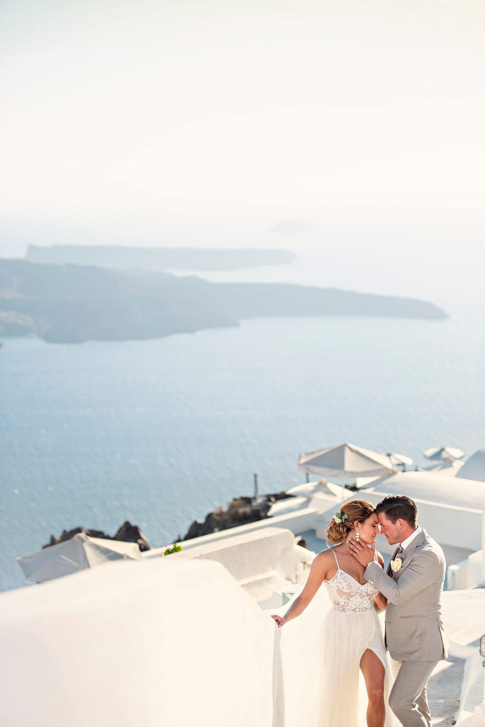Couple shares an intimate moment against white buildings and blue sea views in Santorini, Greece.