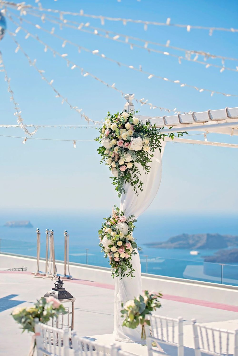Elegant wedding ceremony setup with floral arch and white chairs overlooking a stunning Mediterranean coastal view.