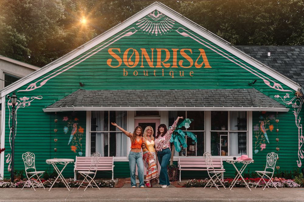 Green exterior of Sonrisa boutique with white trim and outdoor seating area.