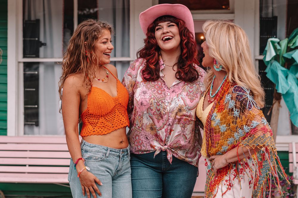 Group wearing colorful summer outfits standing outside a green boutique building.