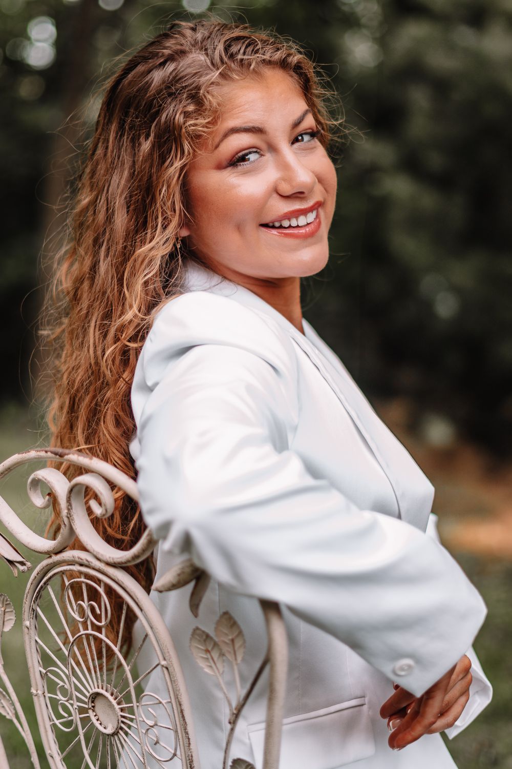 Outdoor portrait series featuring woman in white blazer seated on ornate metal chair.