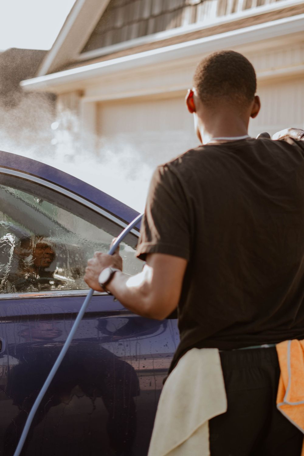 Car detailer spraying water while cleaning vehicle window in driveway.