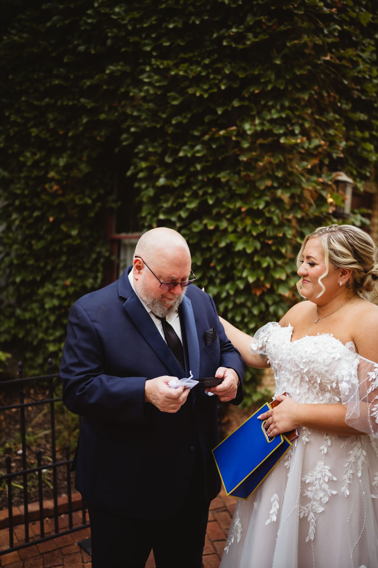 Wedding couple in formal attire reenacting drinking from tiny cups while maintaining social distance during pandemic.