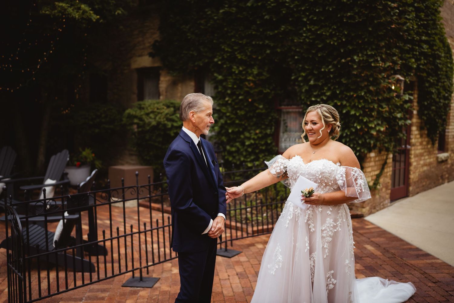 Romantic wedding couple dance tenderly together in golden sunlight surrounded by brick architecture and garden foliage.
