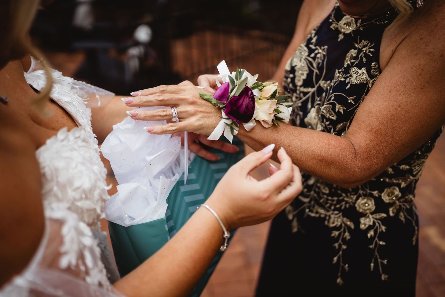 Someone pins a purple and white floral corsage wristlet onto another person wearing a black and gold patterned dress.