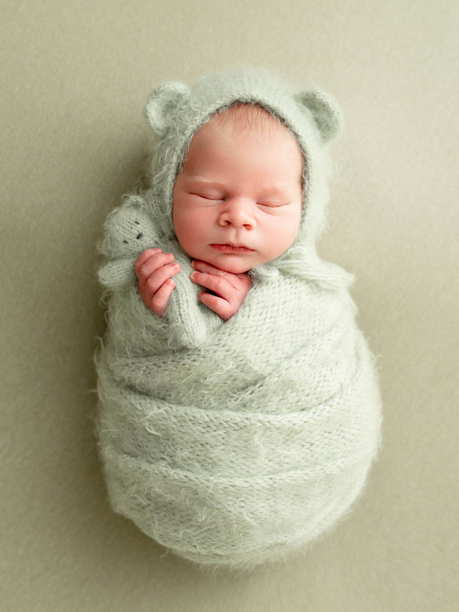 Sleeping newborn wrapped in soft mint green knit blanket photographed from different angles in minimalist style.