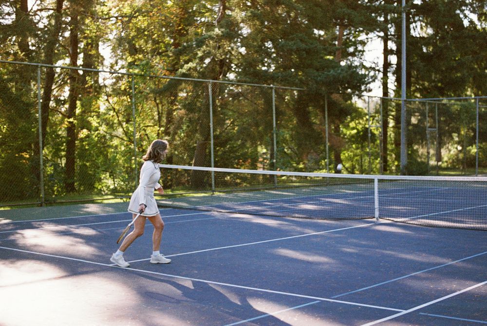 A picturesque sunset illuminates a tennis court surrounded by tall pine trees as players enjoy a match.