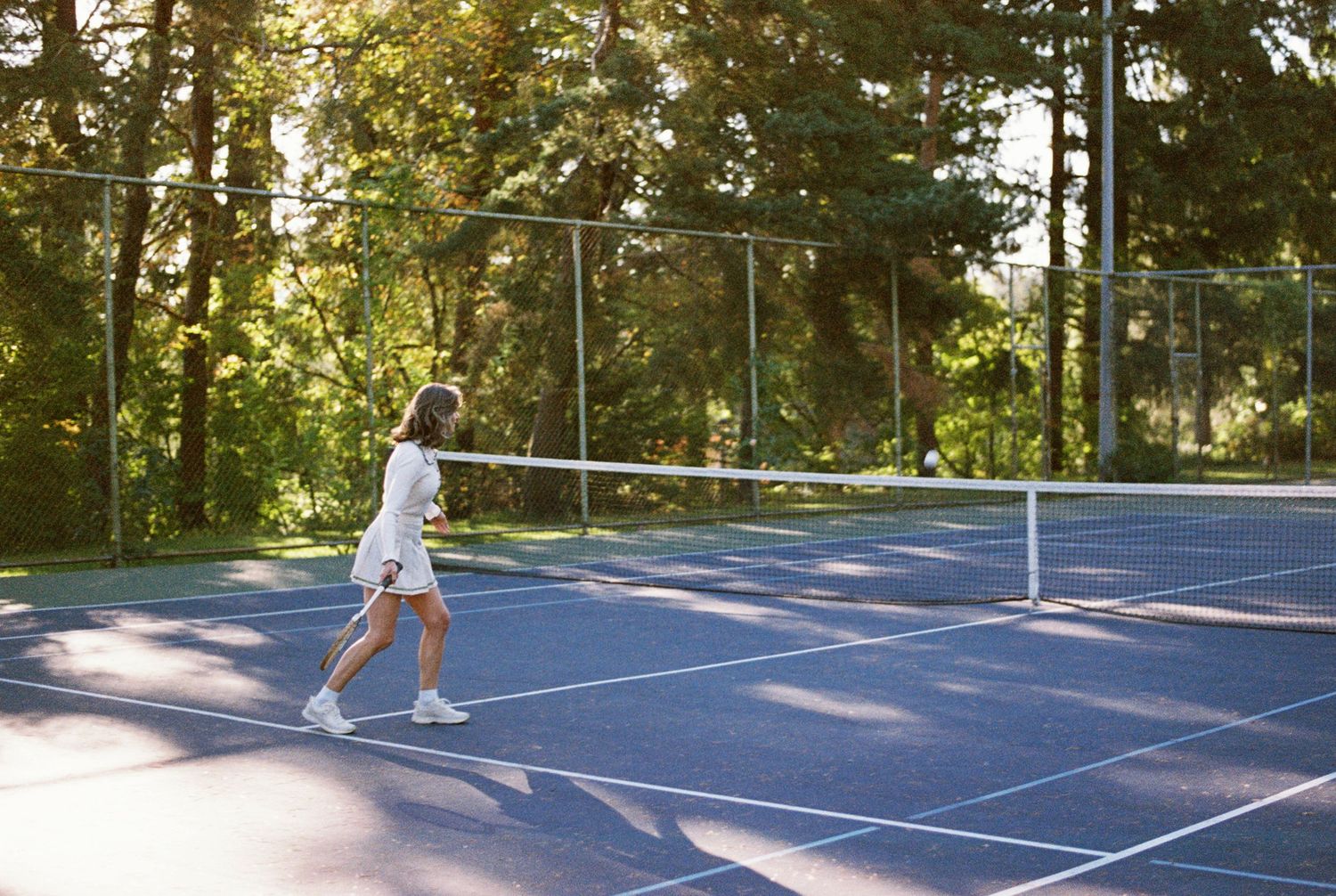 A picturesque sunset illuminates a tennis court surrounded by tall pine trees as players enjoy a match.