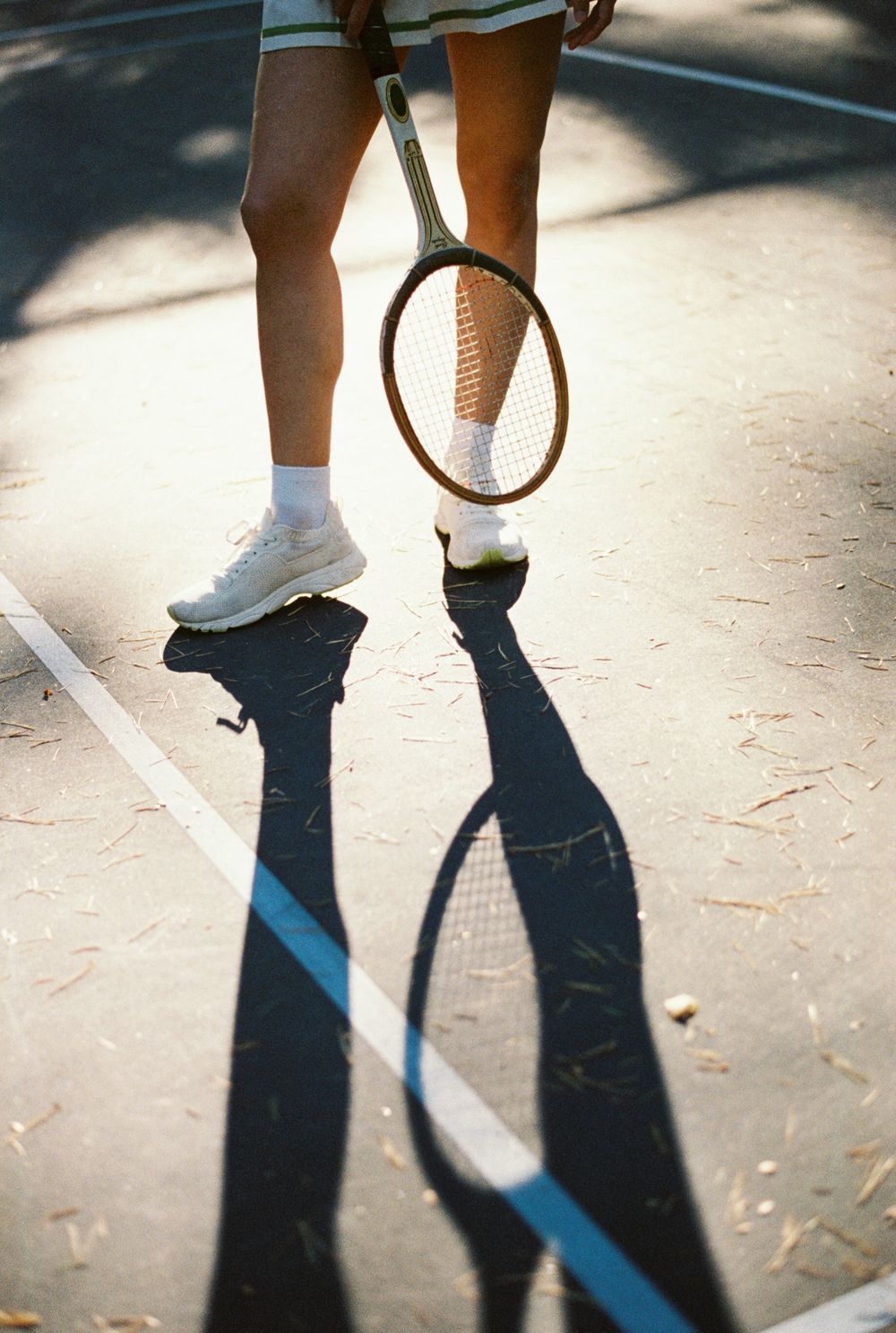 Shadows cast on a tennis court surface show two people playing or dancing together.