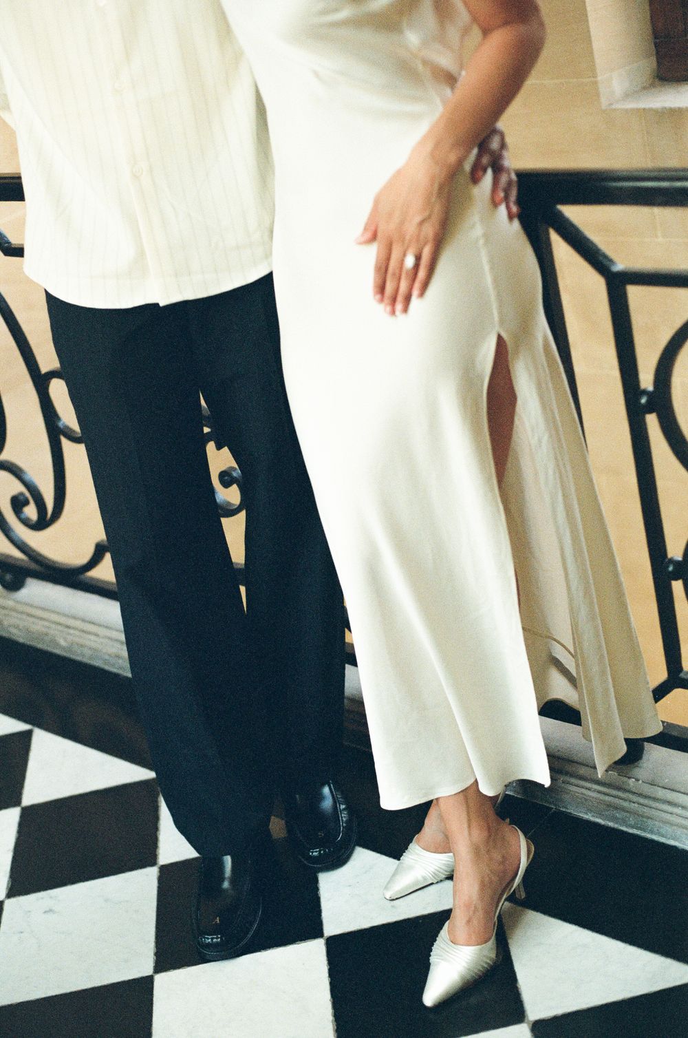 Close-up detail of legs in formal wear with white heels and black pants on checkered floor. Paris film photographer.