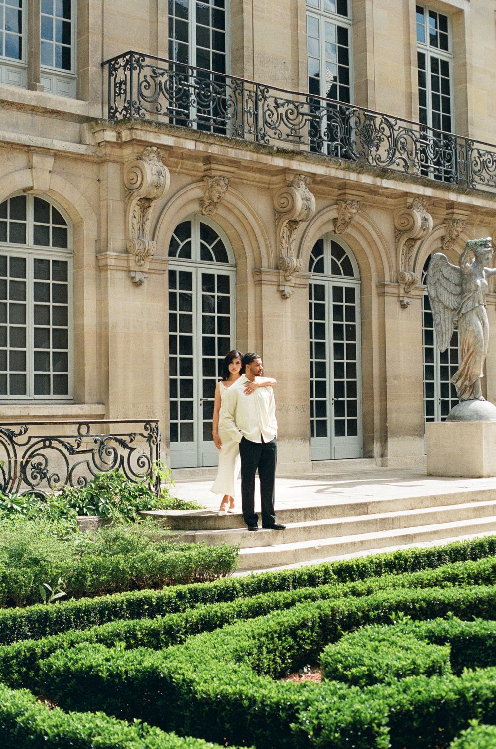 Elegant French-style architectural facade with ornate balconies and manicured hedge garden. Paris film photographer.