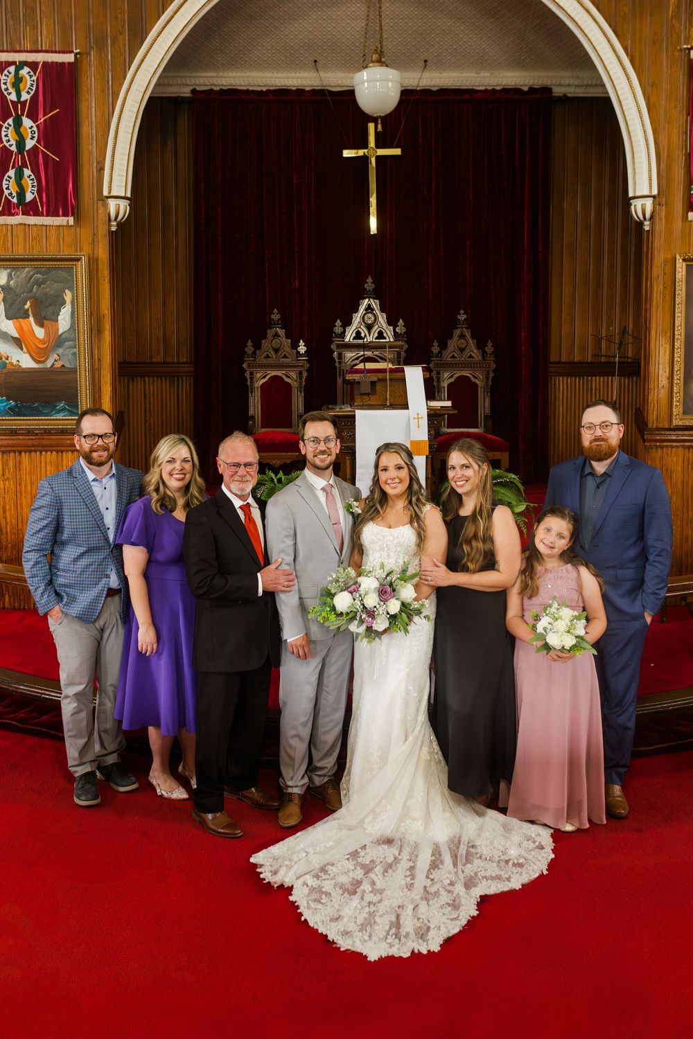 Wedding party lineup in traditional church setting with wood paneling, red carpet and religious decor.