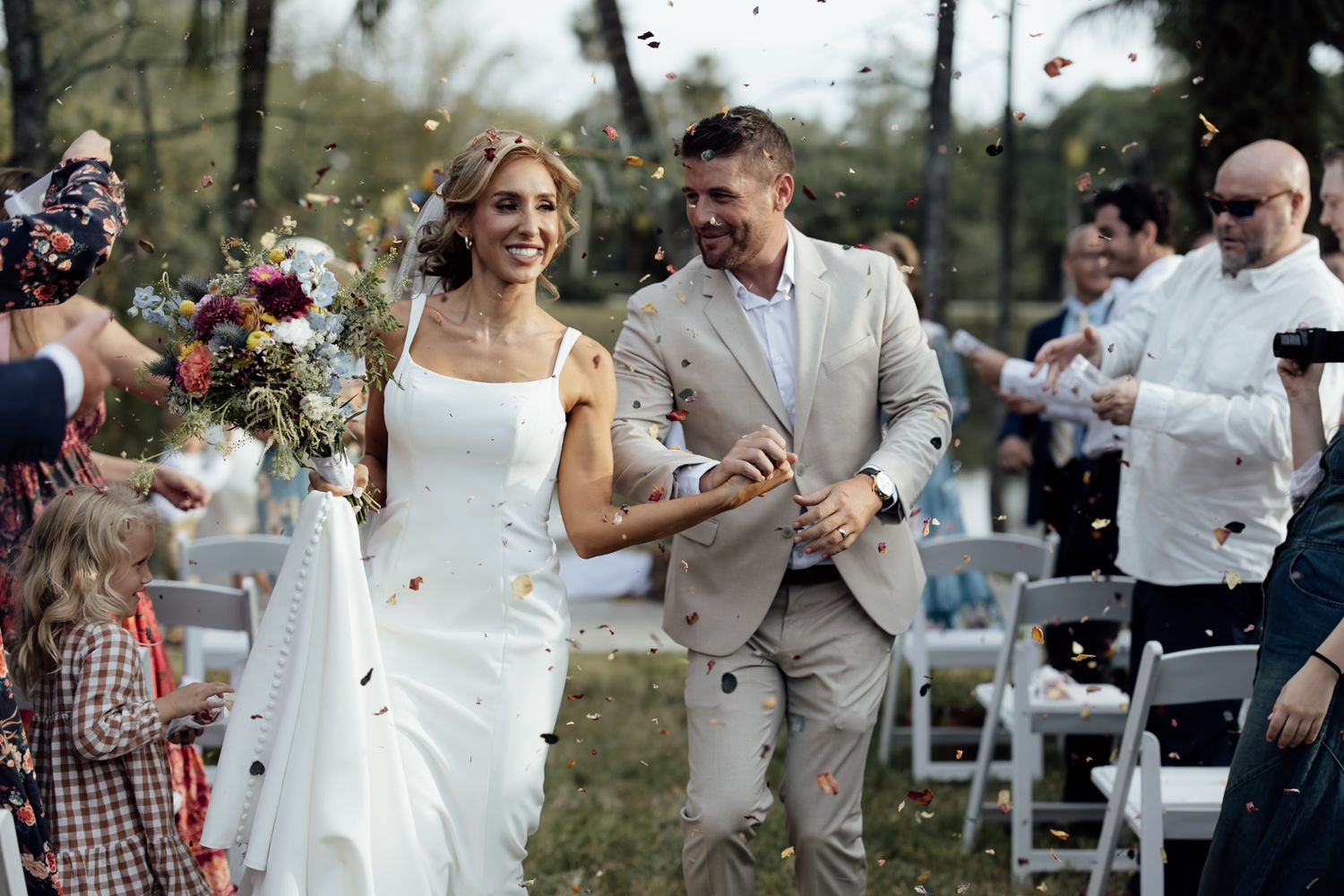 Jupiter Farms wedding photo gallery. Wedding party celebrates with confetti, dancing, and laughter at lakefront, tropical, garden.