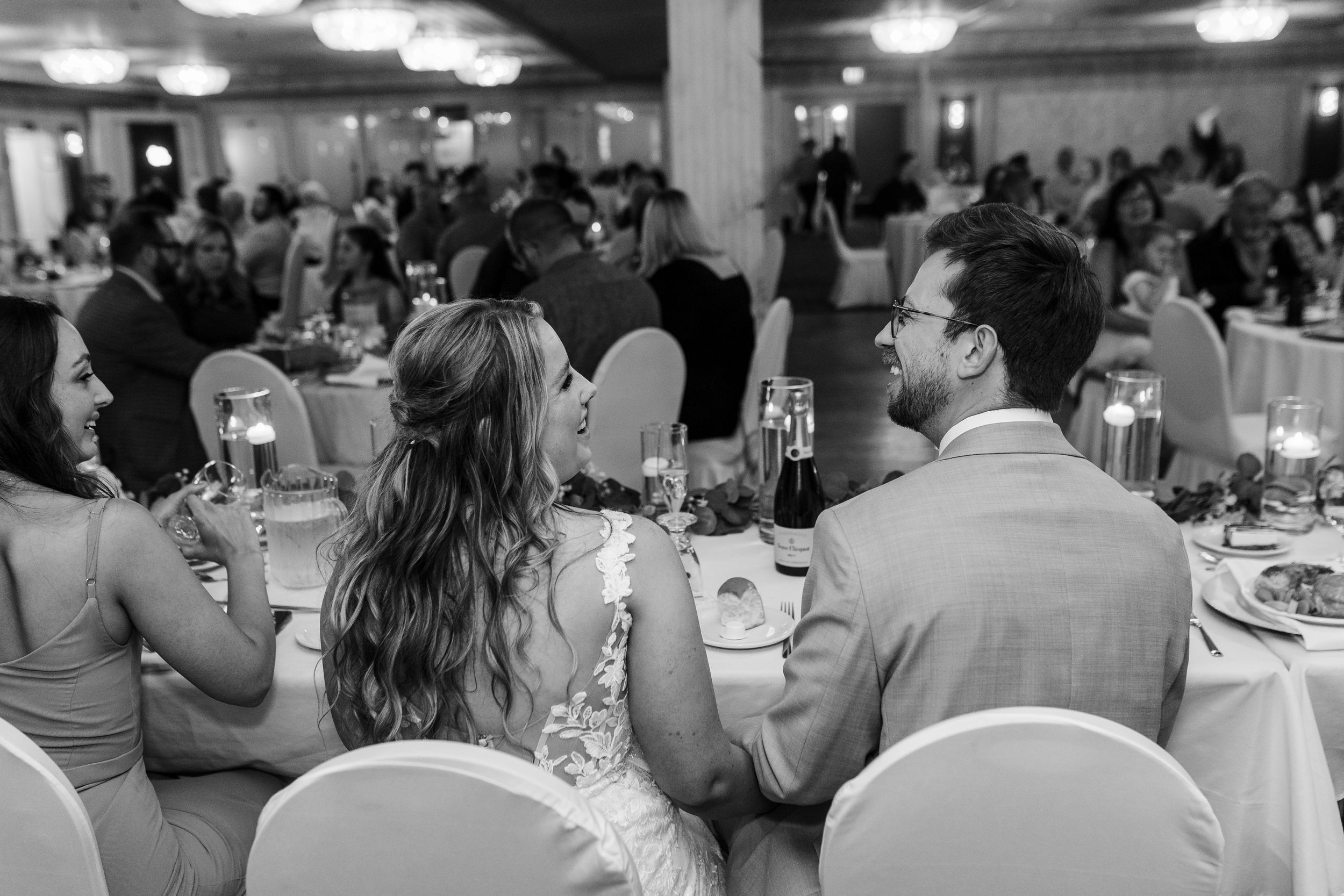People sitting at formal tables during a banquet event in a large indoor venue with bright overhead lighting.