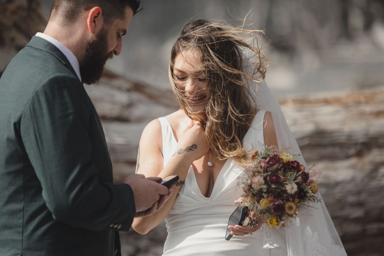 A bride in white dress holds a autumn-colored bouquet while sharing a moment with her partner outdoors.