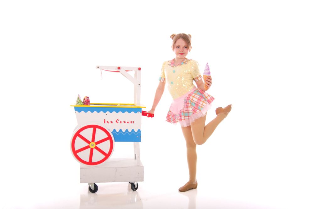 Dance students pose with colorful props and toy carts against white background.