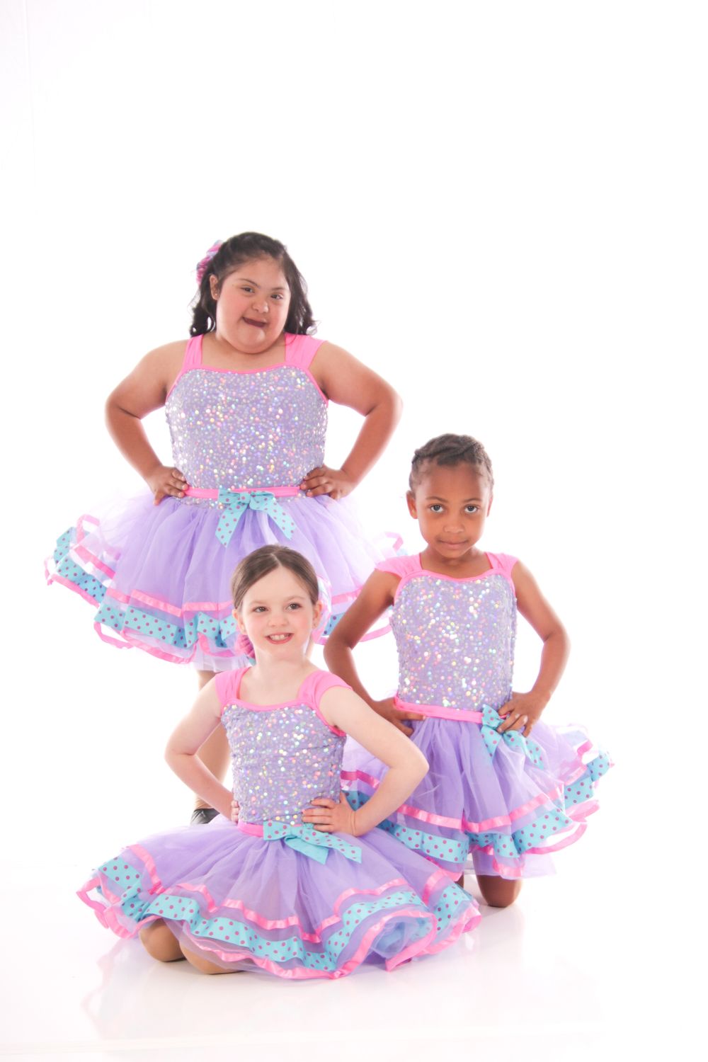 Group of dancers in purple sparkly dresses pose together for recital photo.