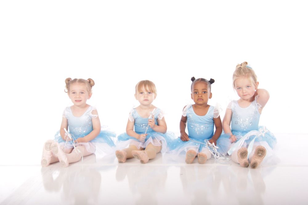 Young ballet students in light blue tutus practicing floor positions together.