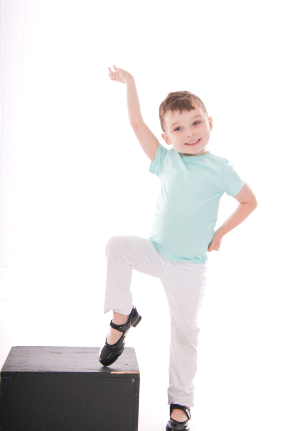 Young performer in mint shirt and white pants dancing energetically on black platform.