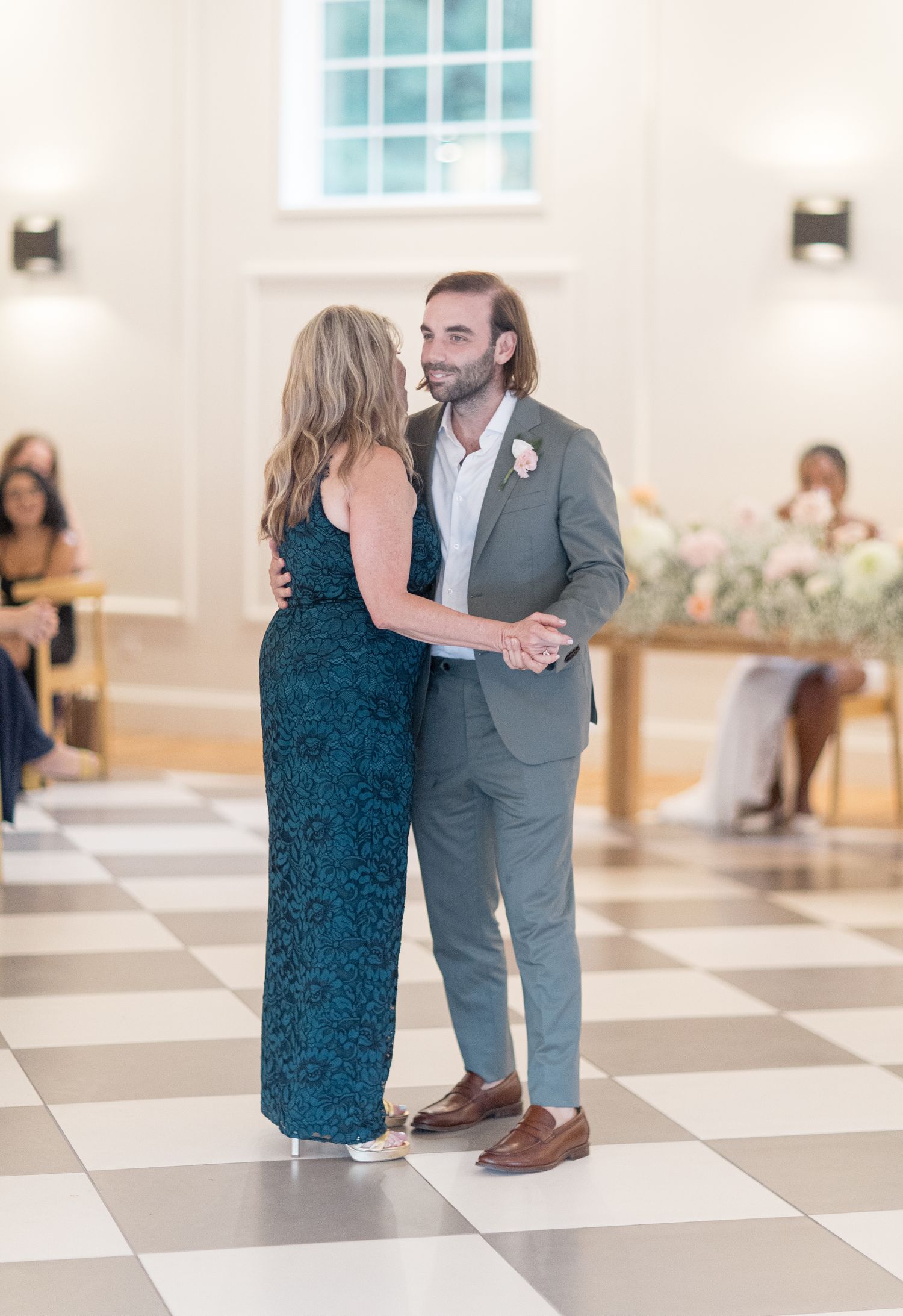 On a black and white checkered floor, a dancing duo in formal wear moves gracefully during a celebratory event.