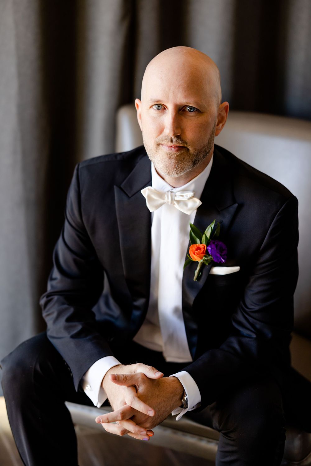 Formal portrait of a groom in a black tuxedo and white bowtie with boutonniere.