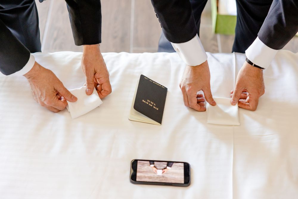 Multiple hands reaching toward a phone and prayer book on a white surface.