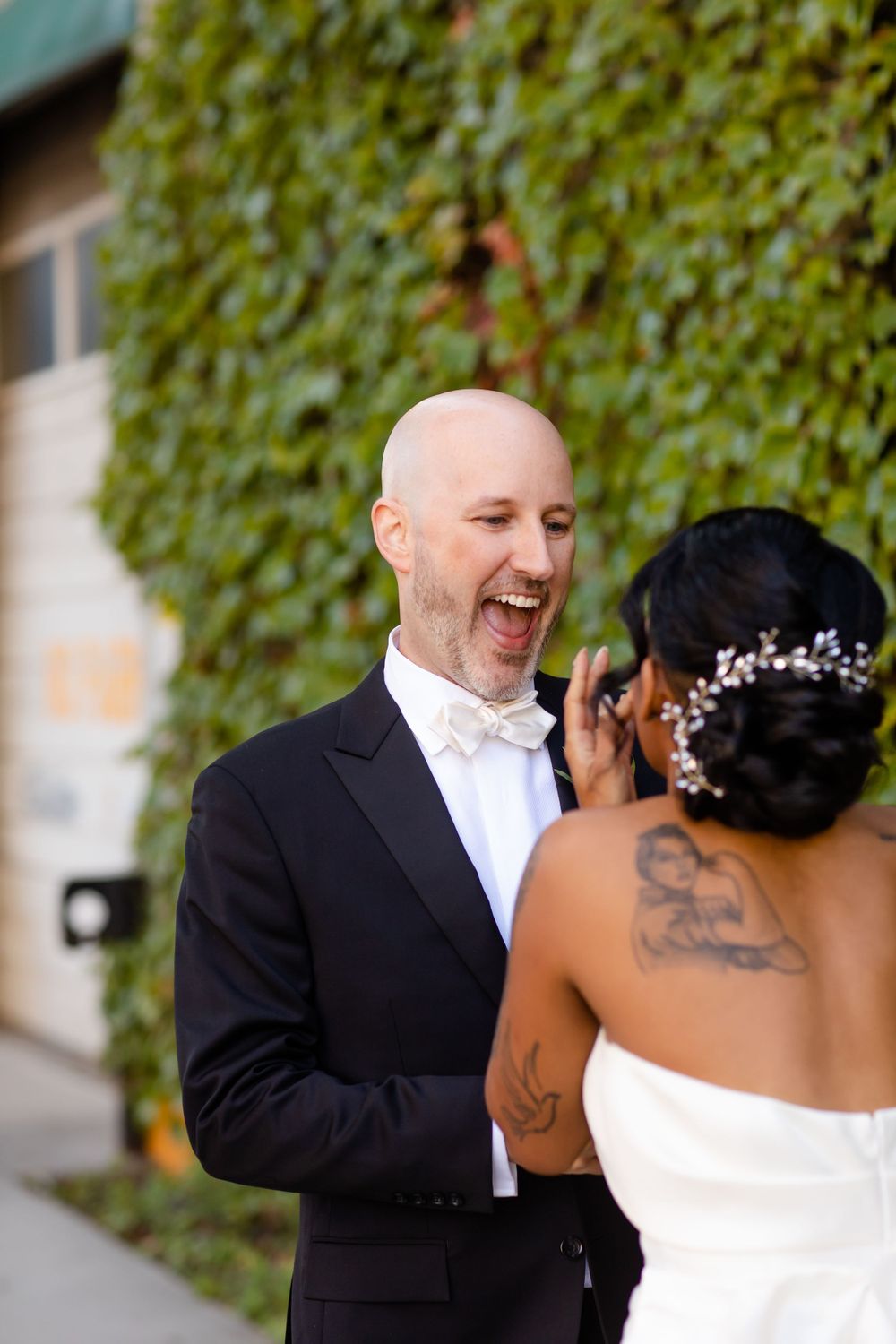 A joyful moment shared between newlyweds in front of an ivy-covered wall.