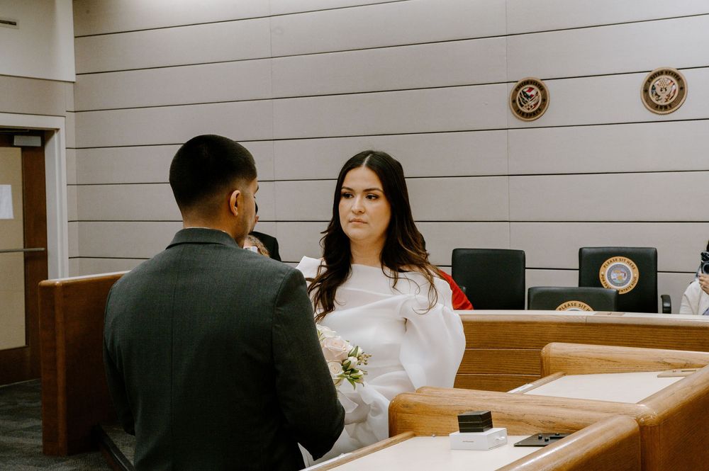 Two people sit in a wooden paneled room with plates and flowers on a table during what appears to be a meal service.