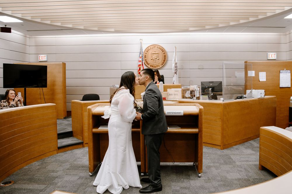 Wide angle view of a wood-paneled courtroom interior showing seating areas and legal proceedings.