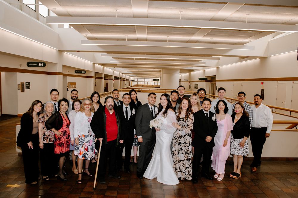 Large wedding party group poses together in formal attire in a hallway with wood paneled walls.