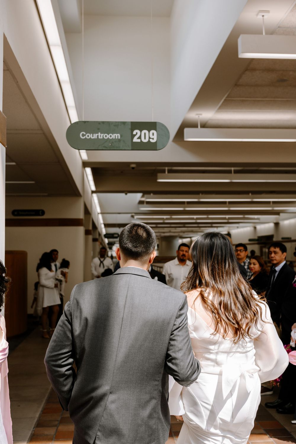 Group of people walking through hallway towards Courtroom 209 sign visible at end of corridor.