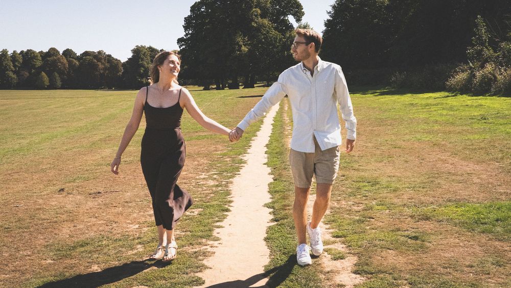 A couple walking together on a dirt path through a sunny meadow on a summer day.