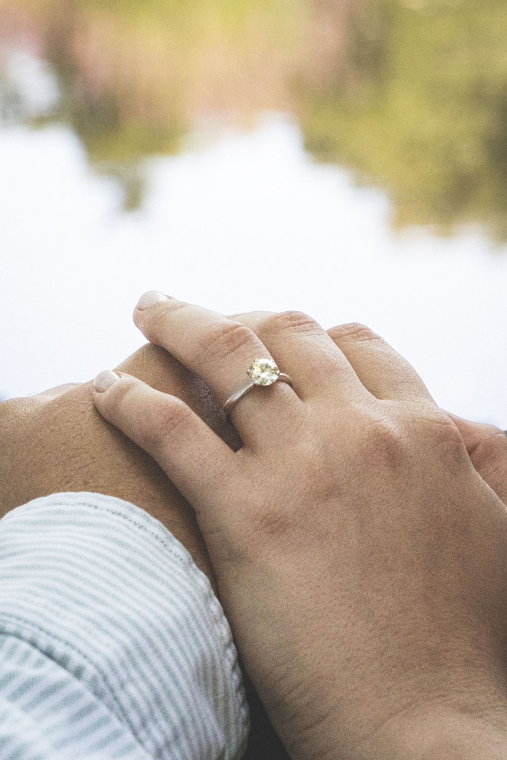 Close-up of hands with an engagement ring resting together against a soft, blurred background.