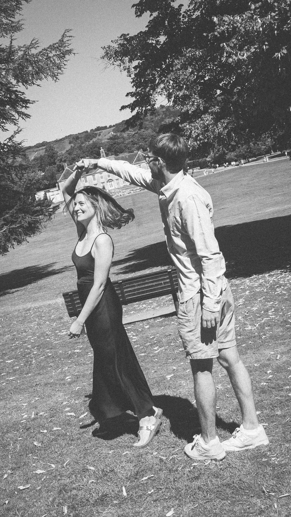 A black and white photo of two people dancing playfully in a grassy outdoor setting.