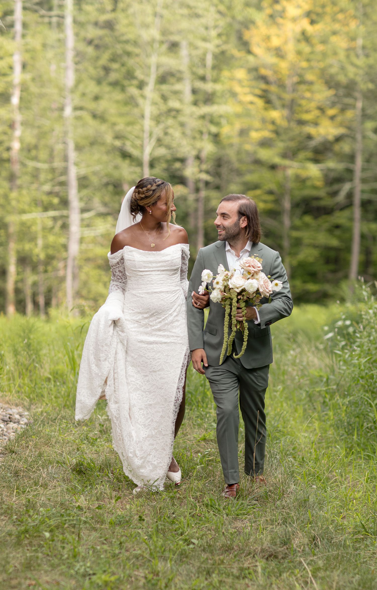 Couple dancing together in a forest clearing wearing wedding attire on a sunny autumn day.