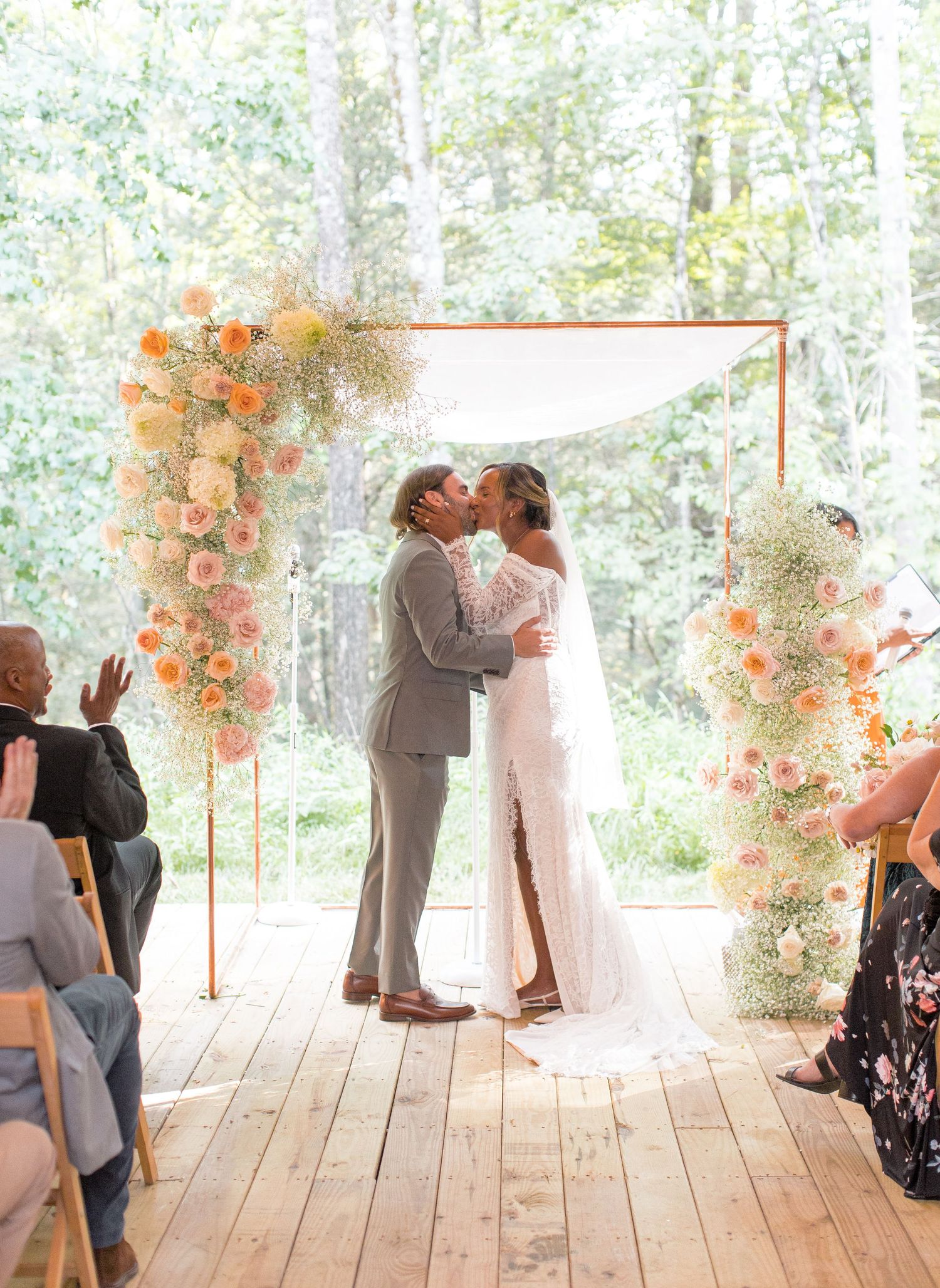 Couple dancing and embracing during a wedding ceremony on a wooden deck surrounded by autumn floral arrangements.
