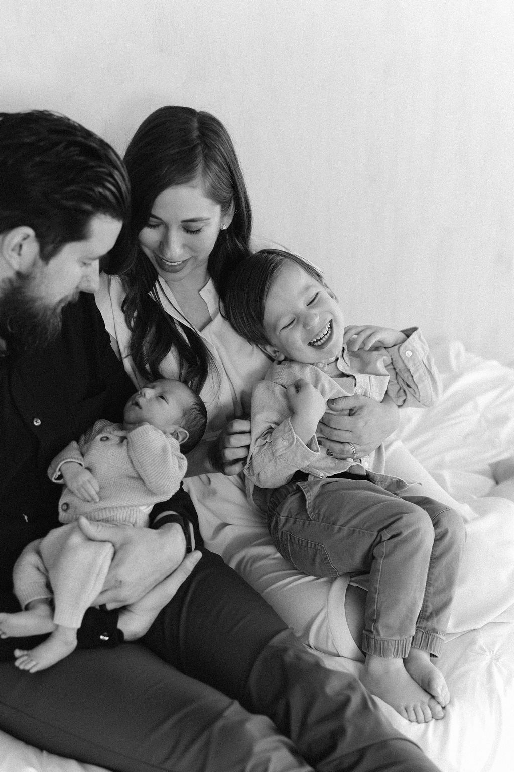 A joyful family moment captured in black and white as they cuddle and laugh together on a bed.