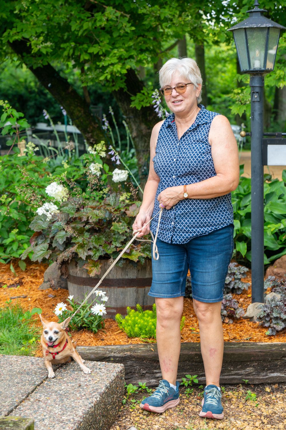 A person wearing a polka dot sleeveless top and denim shorts walks a small dog on a garden path near decorative lampposts. Quad Cities Photo