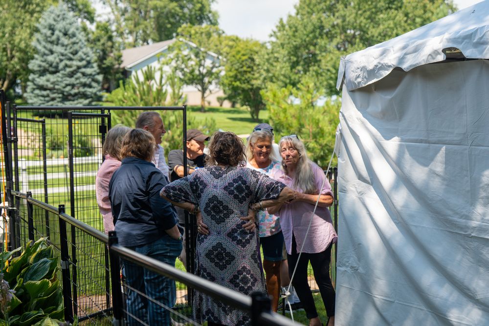 Group of attendees gathered near a white event tent in an outdoor garden setting. Celebration of Life Quad Cities Photography