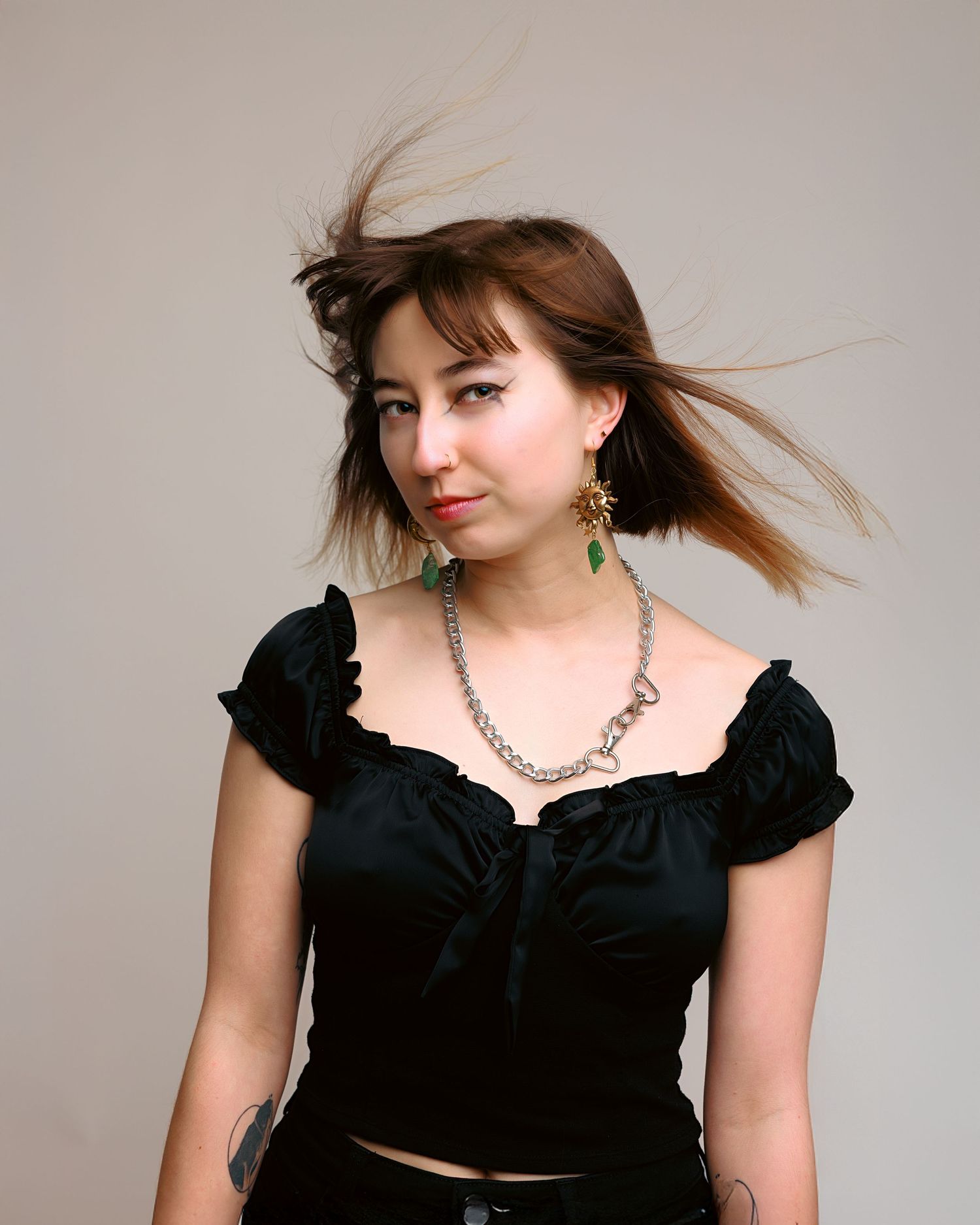 Portrait of someone in black ruffled top with flowing hair and statement necklace against neutral background.