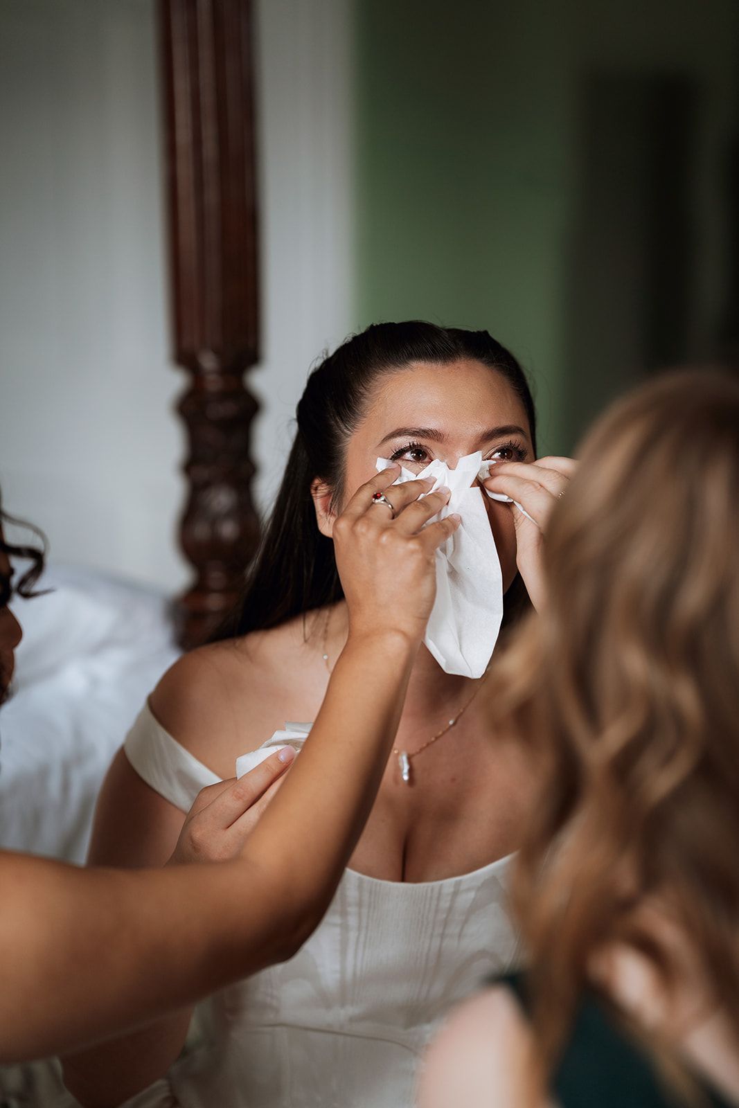 Someone wearing a white dress wipes tears with a tissue during an emotional wedding preparation moment.