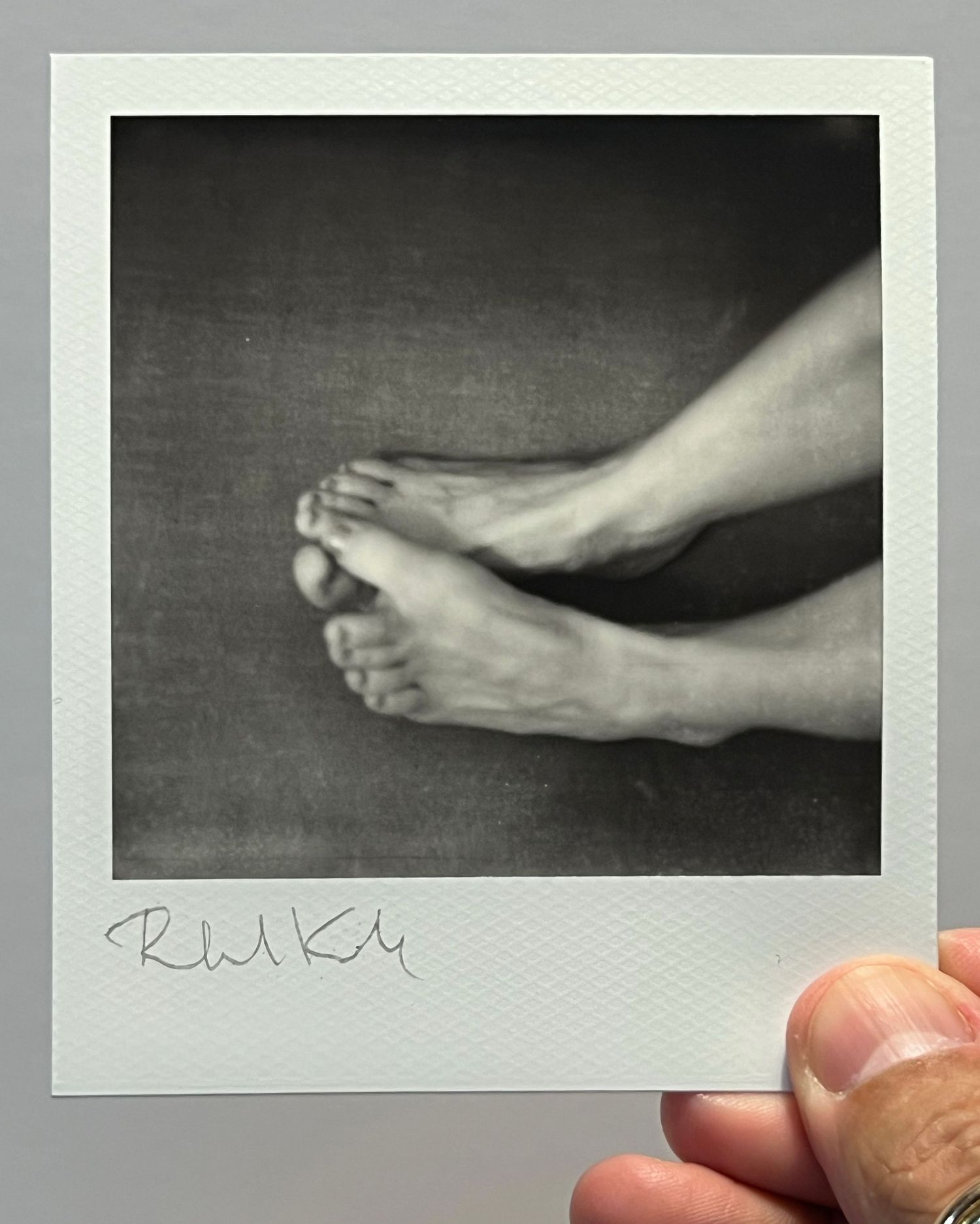 Black and white polaroid photograph showing bare feet against textured surface.