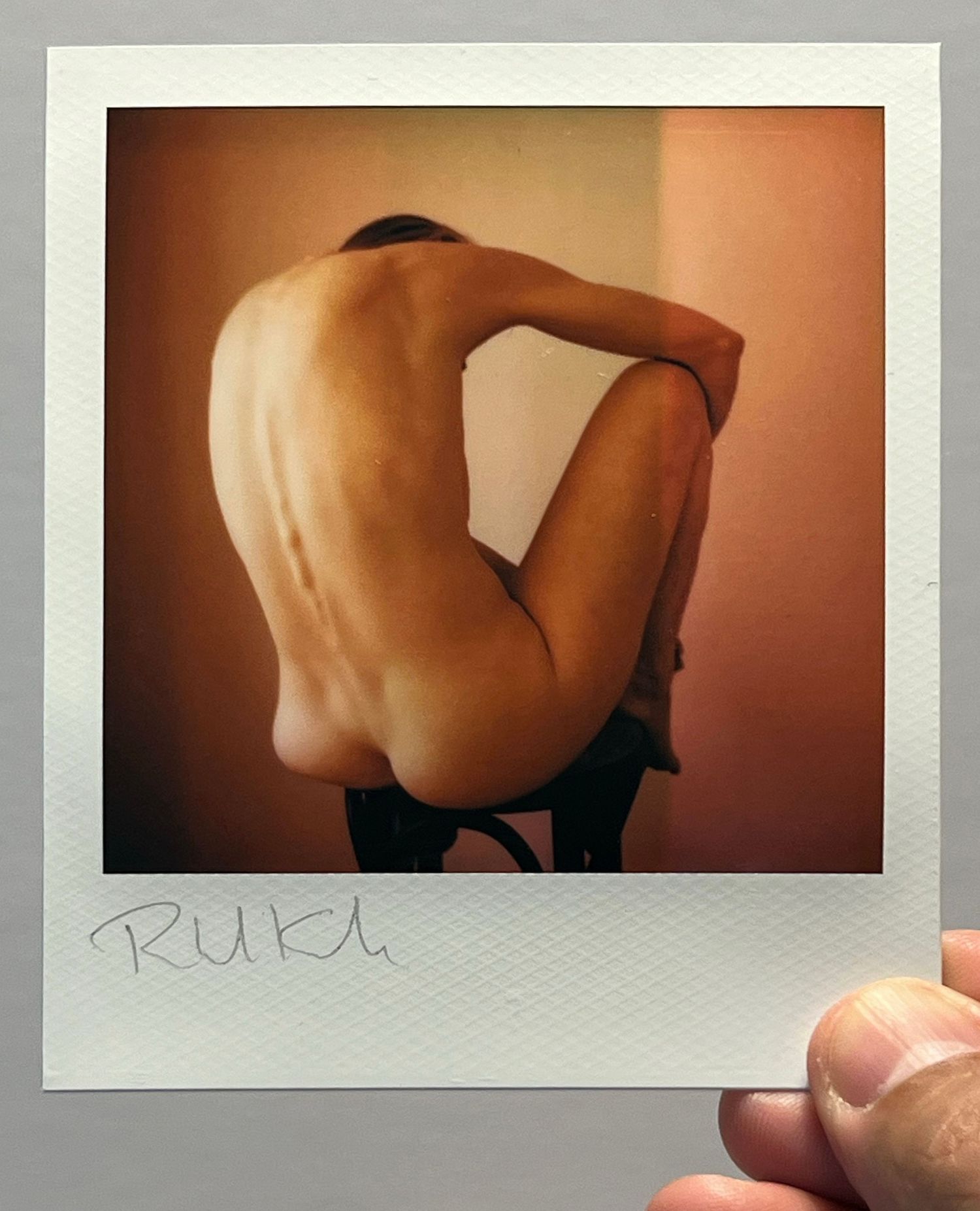 Artistic nude polaroid photograph showing back muscles in warm lighting.