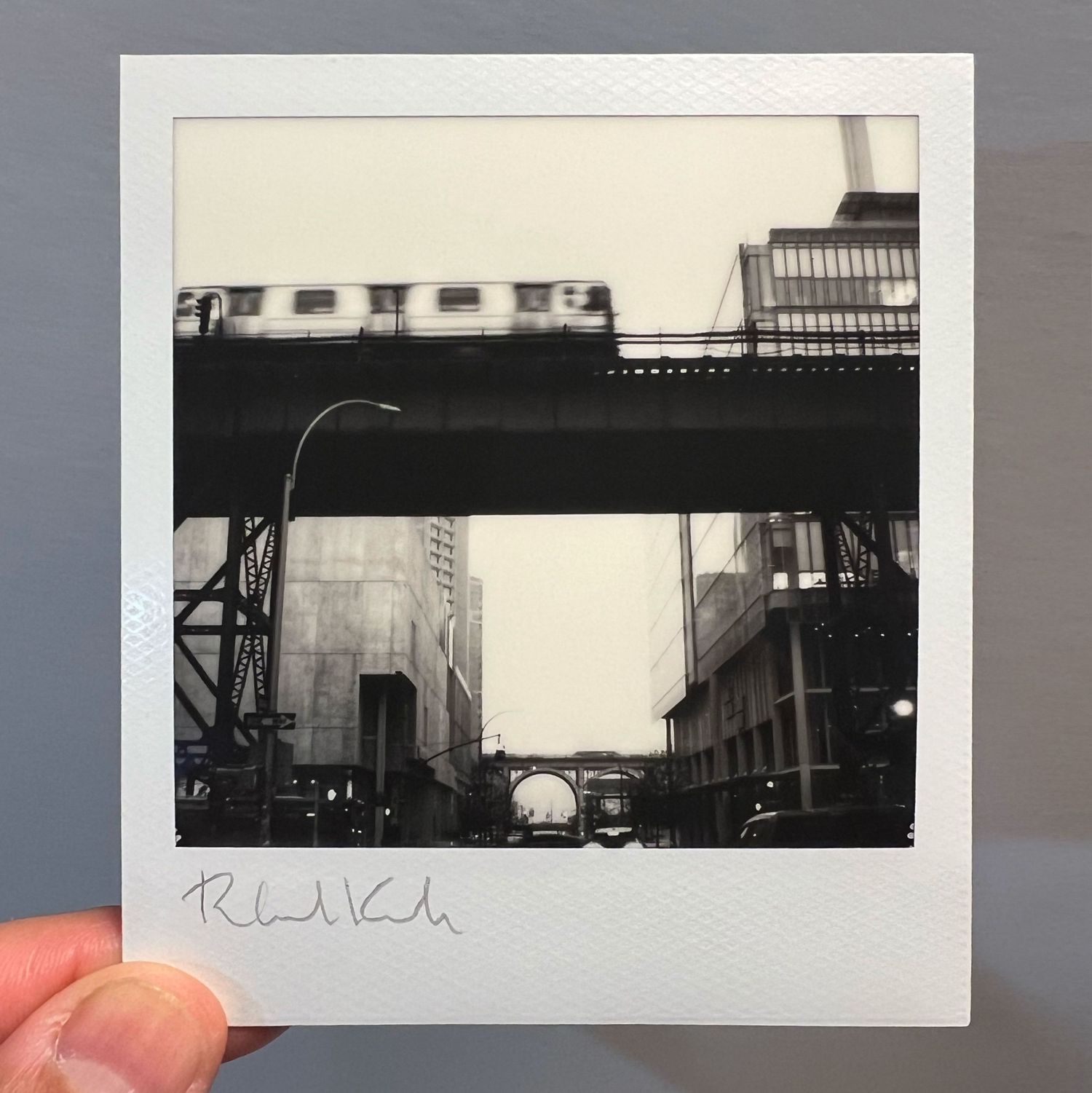 Urban polaroid showing elevated train track with subway car against city buildings.