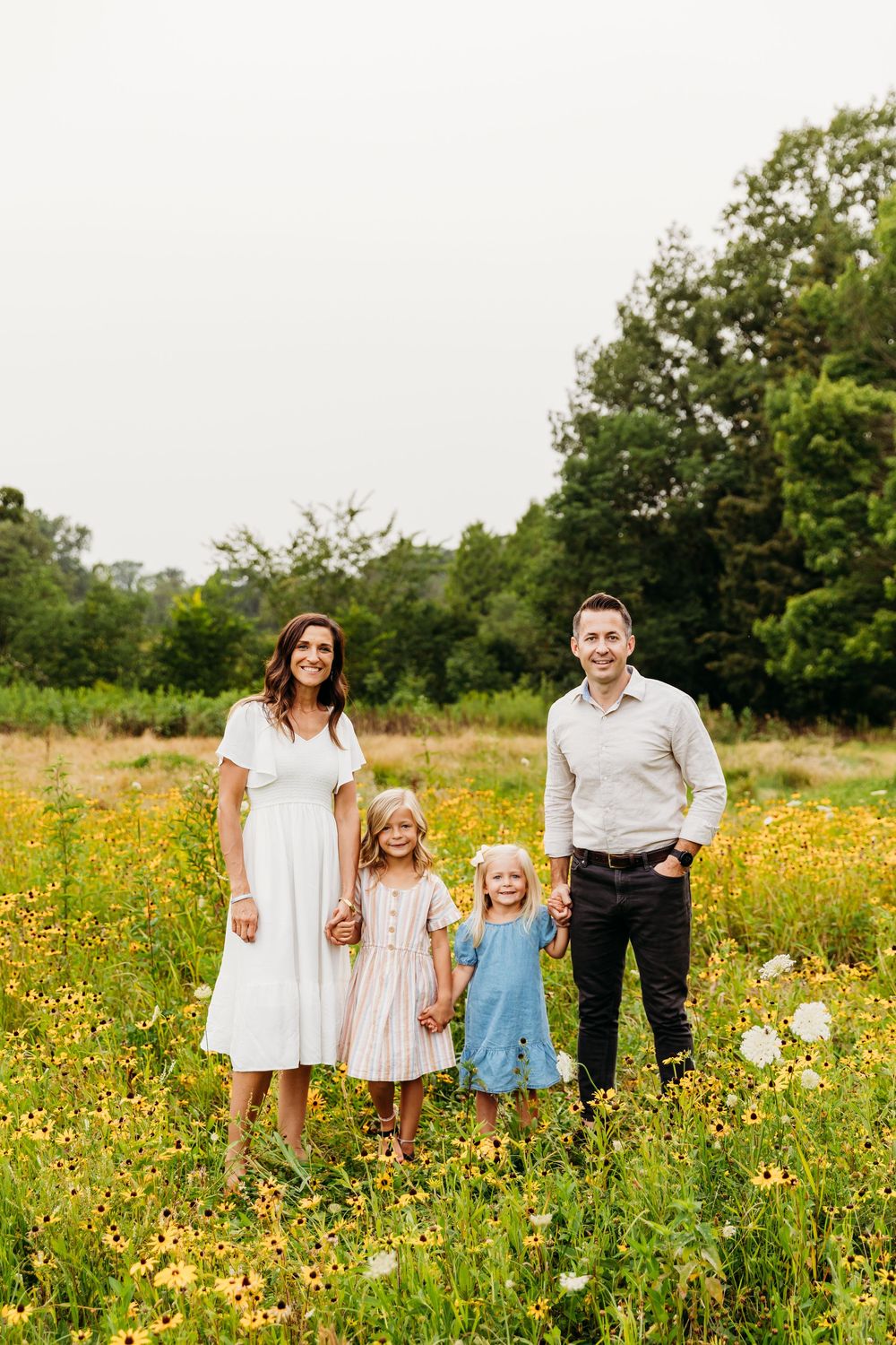A family stands together in a vibrant wildflower meadow filled with yellow blooms on a sunny day.