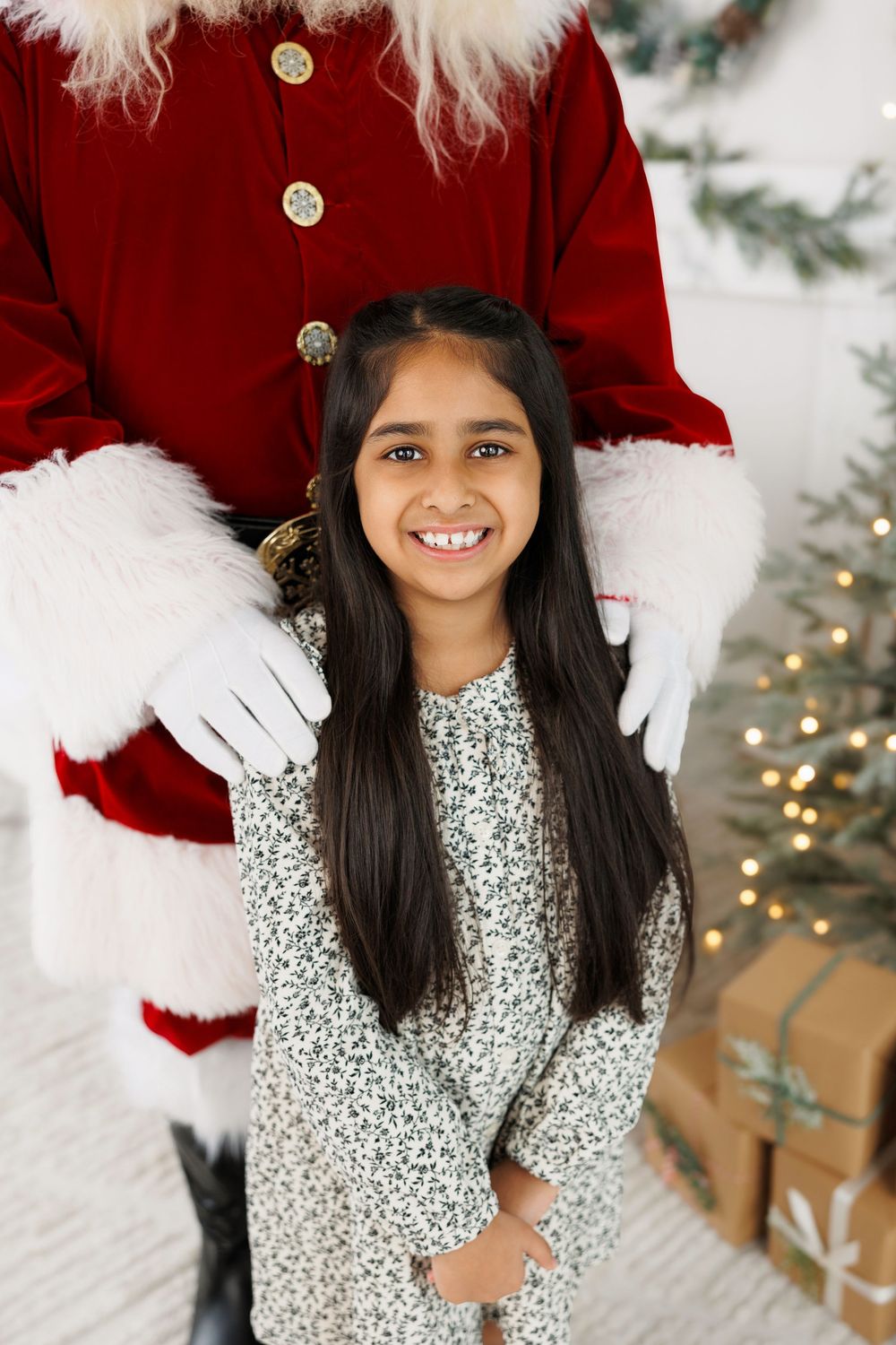 A smiling figure in a silver sequined dress poses in front of a Christmas tree with white-gloved hands visible behind them.