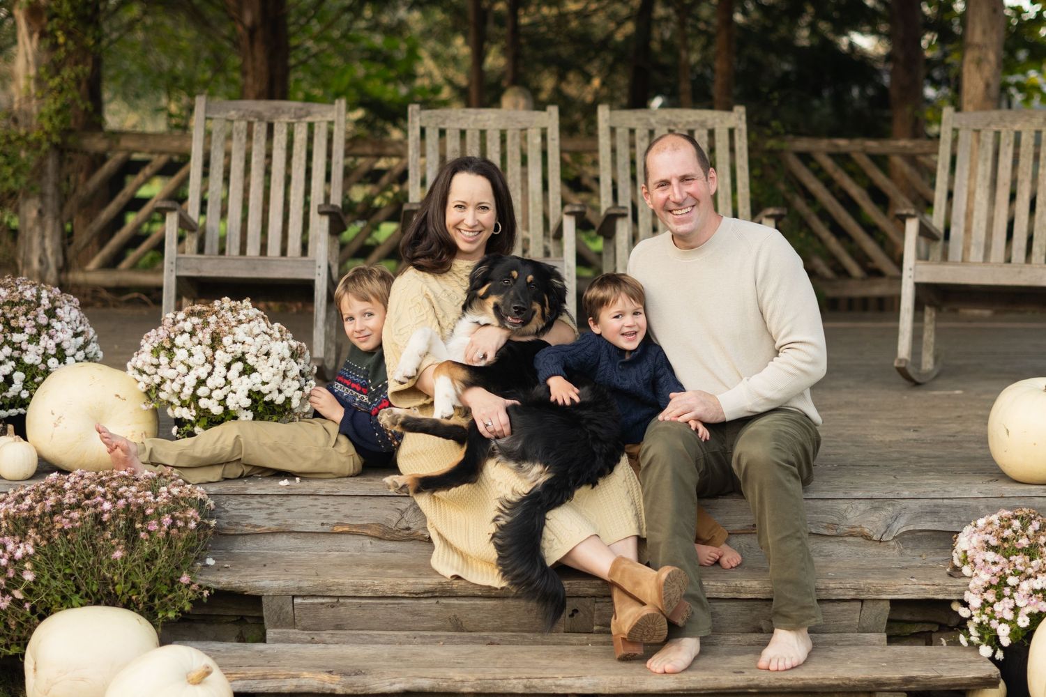 Family relaxes on wooden bench with their fluffy dog on sunny porch in Leiper's Fork for a mini session.